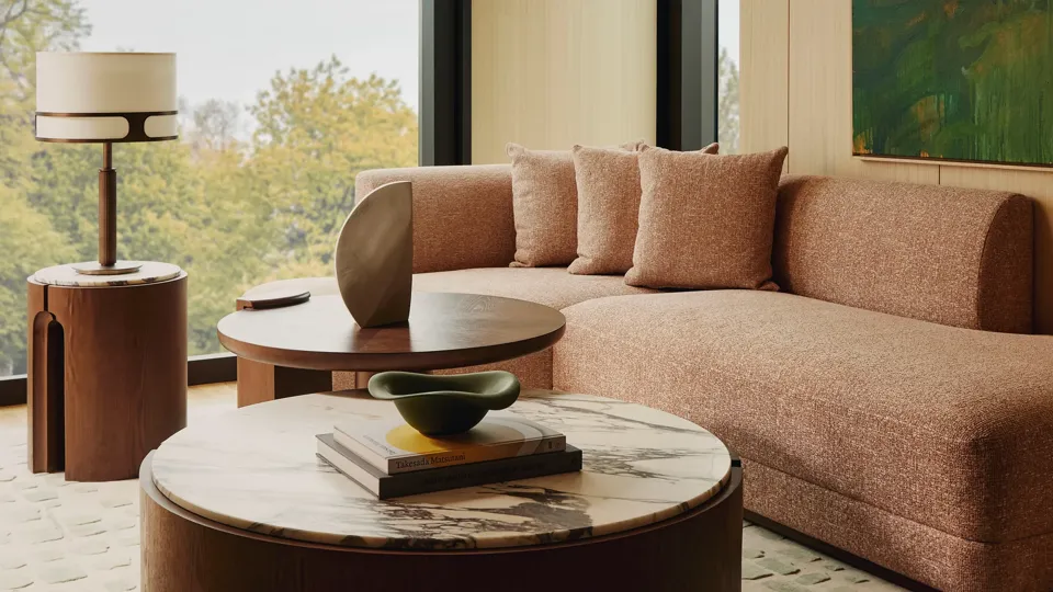 Modern living room with a neutral sectional sofa, large window overlooking green trees.