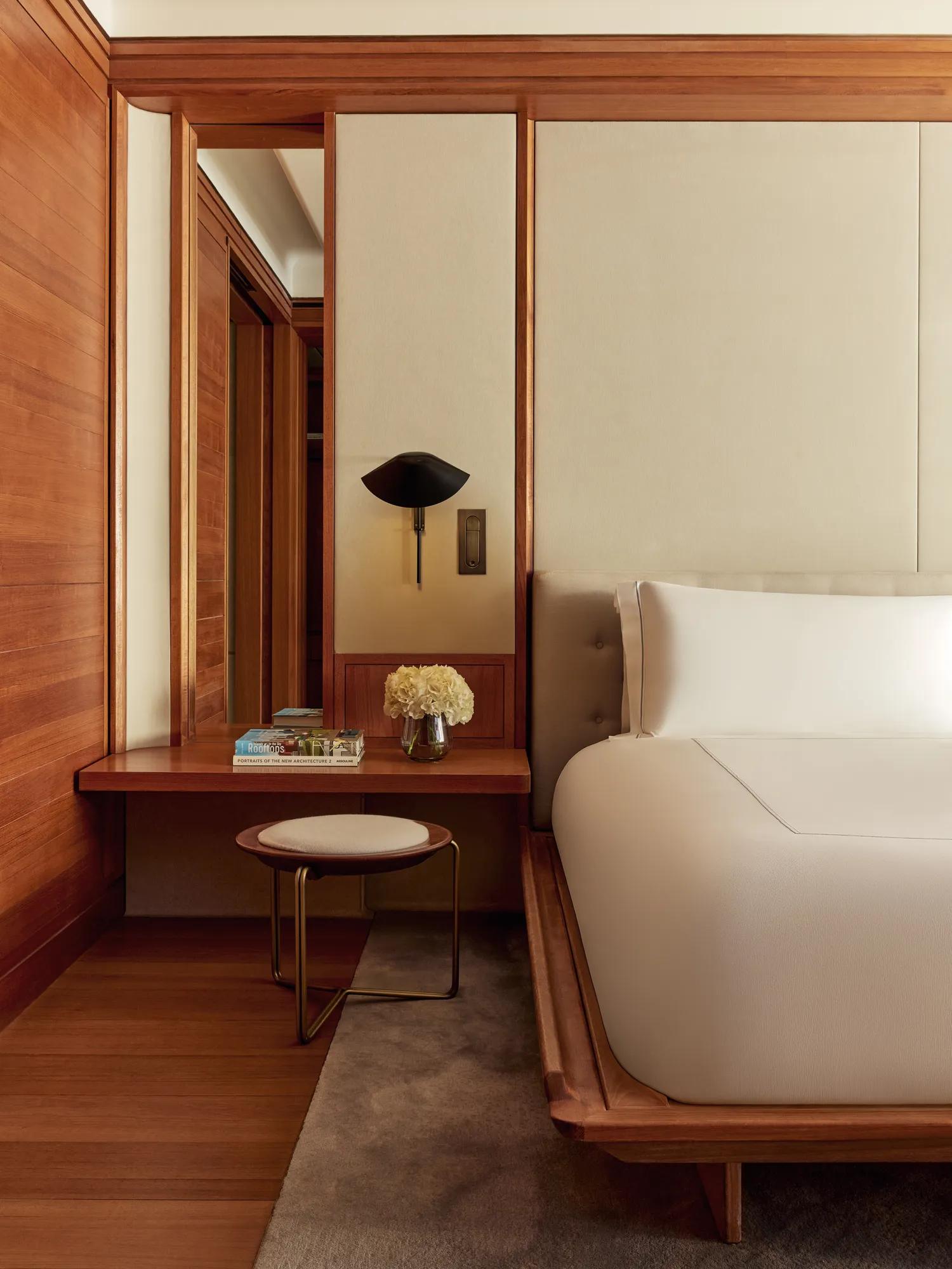 Bedside view of modern suite with built-in desk, stool, fresh flowers, and wooden wall panels
