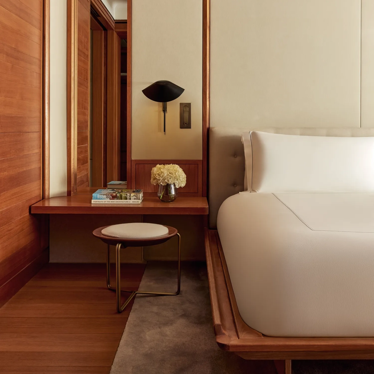 Bedside view of modern suite with built-in desk, stool, fresh flowers, and wooden wall panels