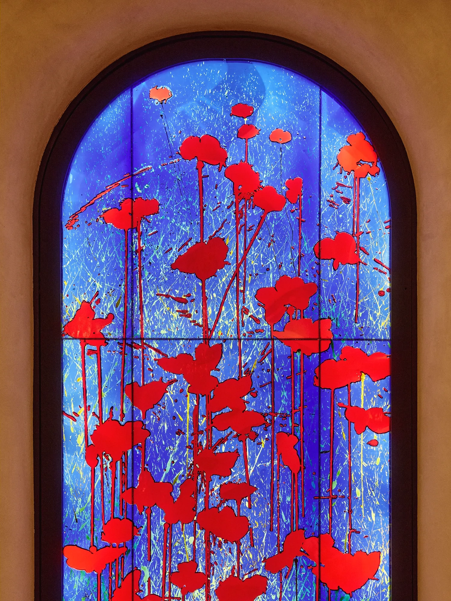 Arched stained-glass-style panel with vivid red poppy silhouettes against a glowing blue background.
