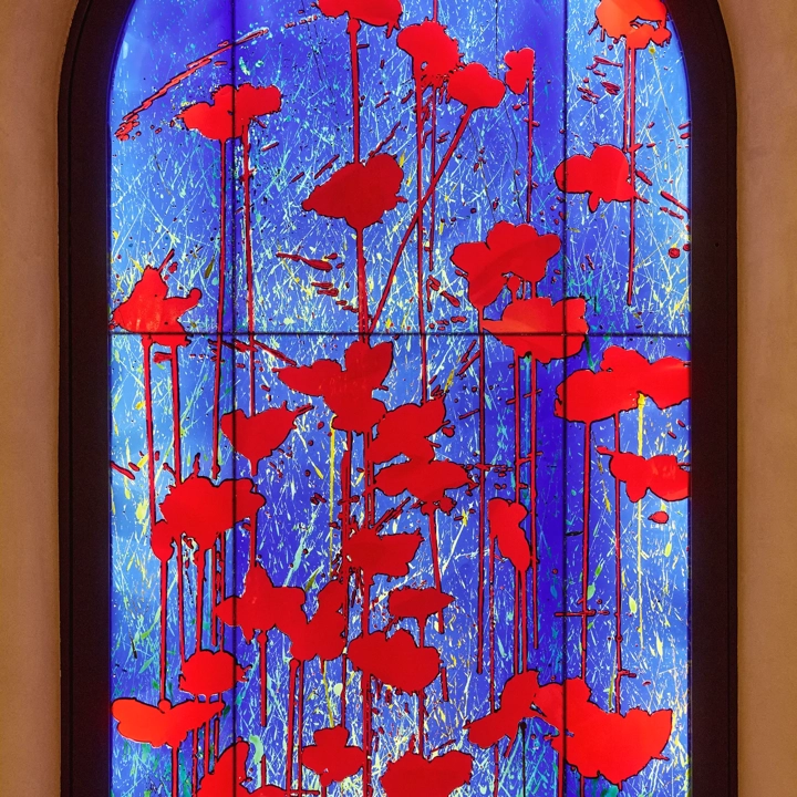 Arched stained-glass-style panel with vivid red poppy silhouettes against a glowing blue background.