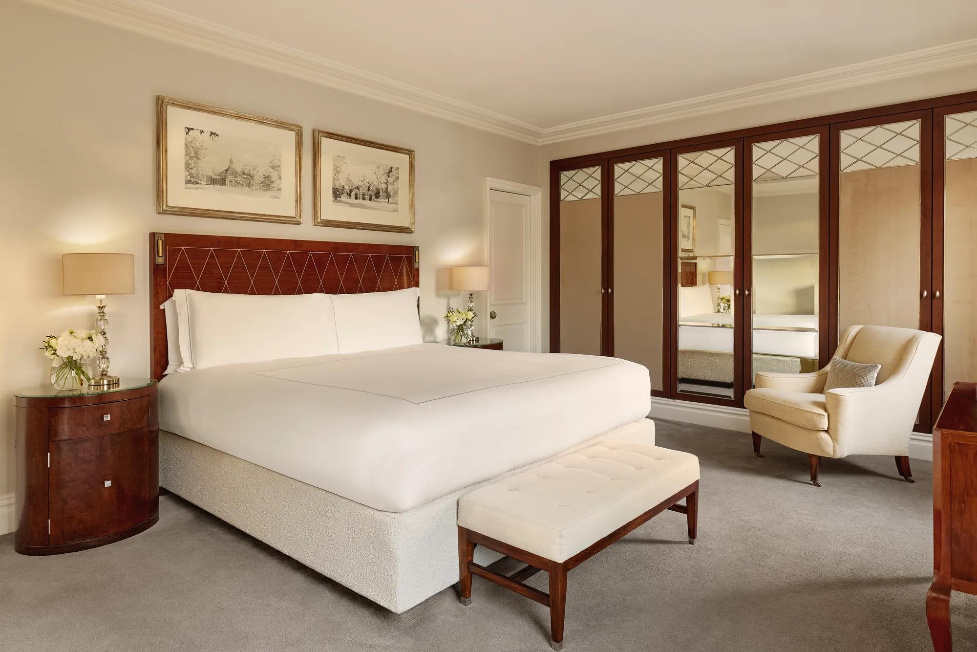 Spacious bedroom featuring a king-size bed with a polished wooden headboard, mirrored wardrobes, and neutral-toned furnishings.