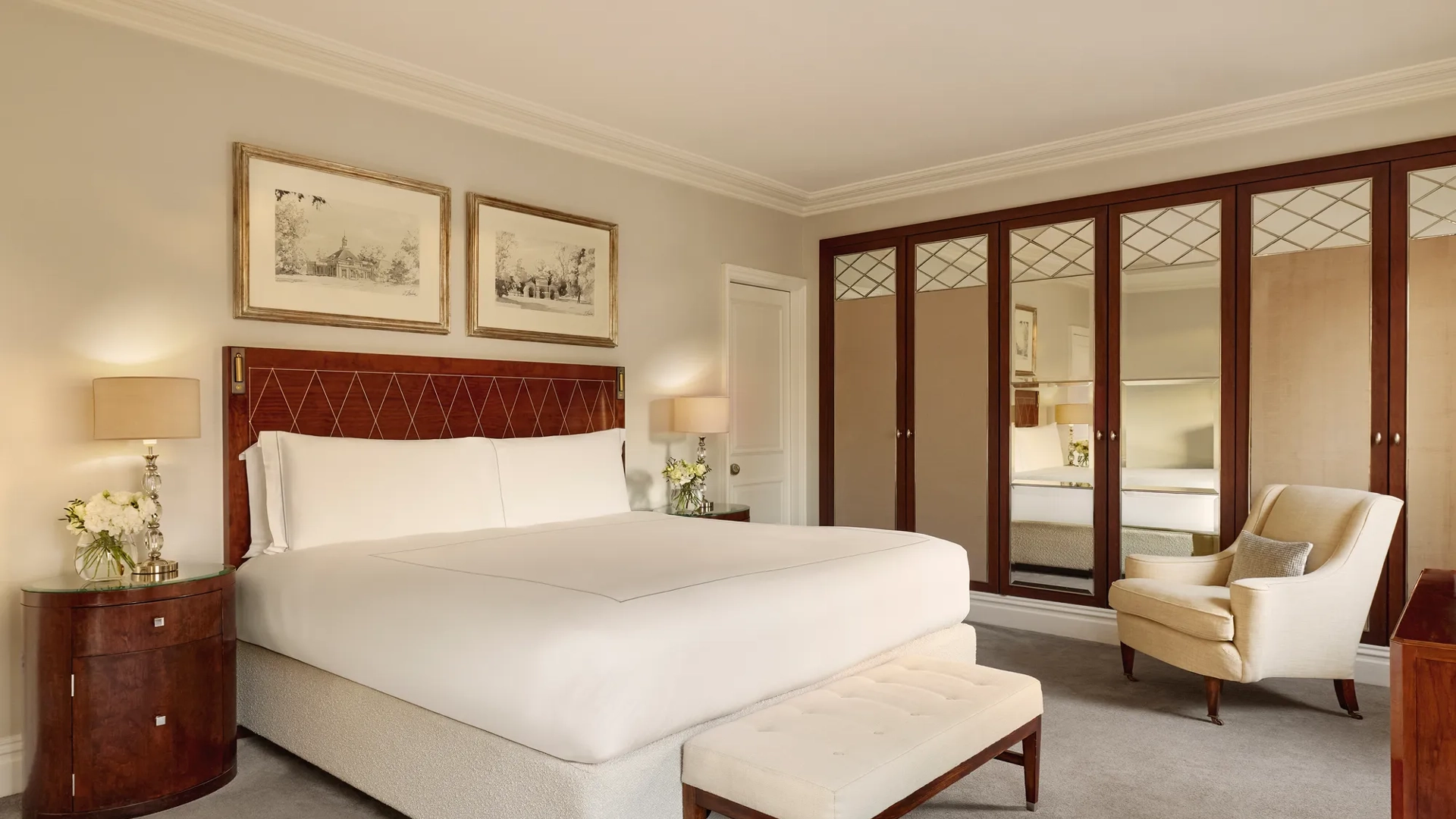 Spacious bedroom featuring a king-size bed with a polished wooden headboard, mirrored wardrobes, and neutral-toned furnishings.