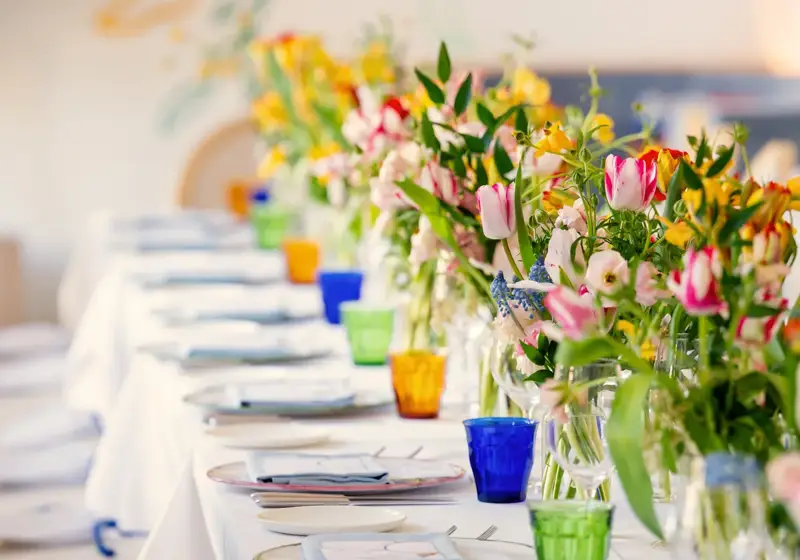 Long private dining table set with colorful glassware and vases of tulips against a mural backdrop.
