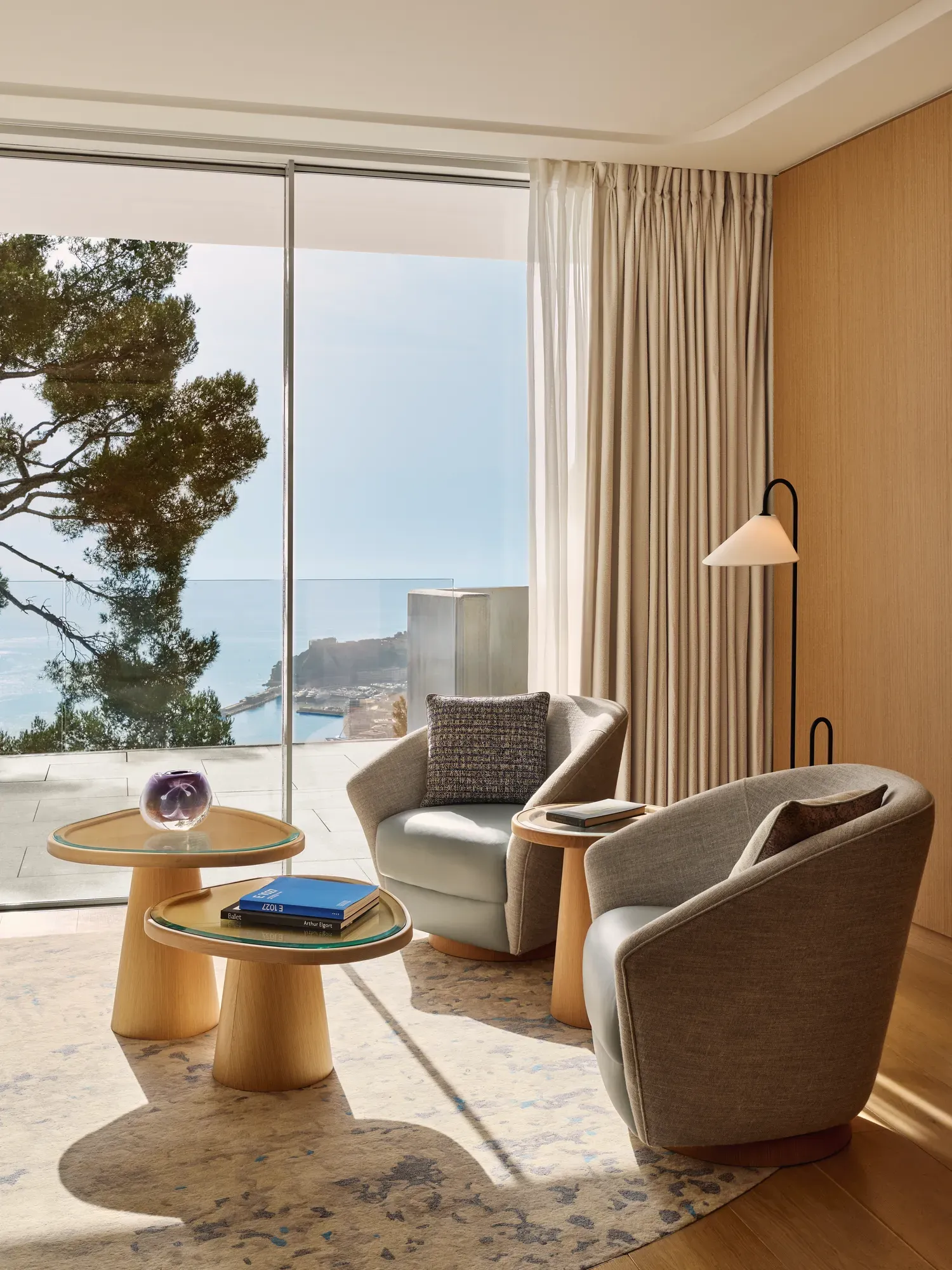 Espace détente avec deux fauteuils et tables d’appoint donnant sur la mer à travers de grandes baies vitrées.