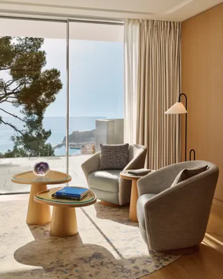 Espace détente avec deux fauteuils et tables d’appoint donnant sur la mer à travers de grandes baies vitrées.