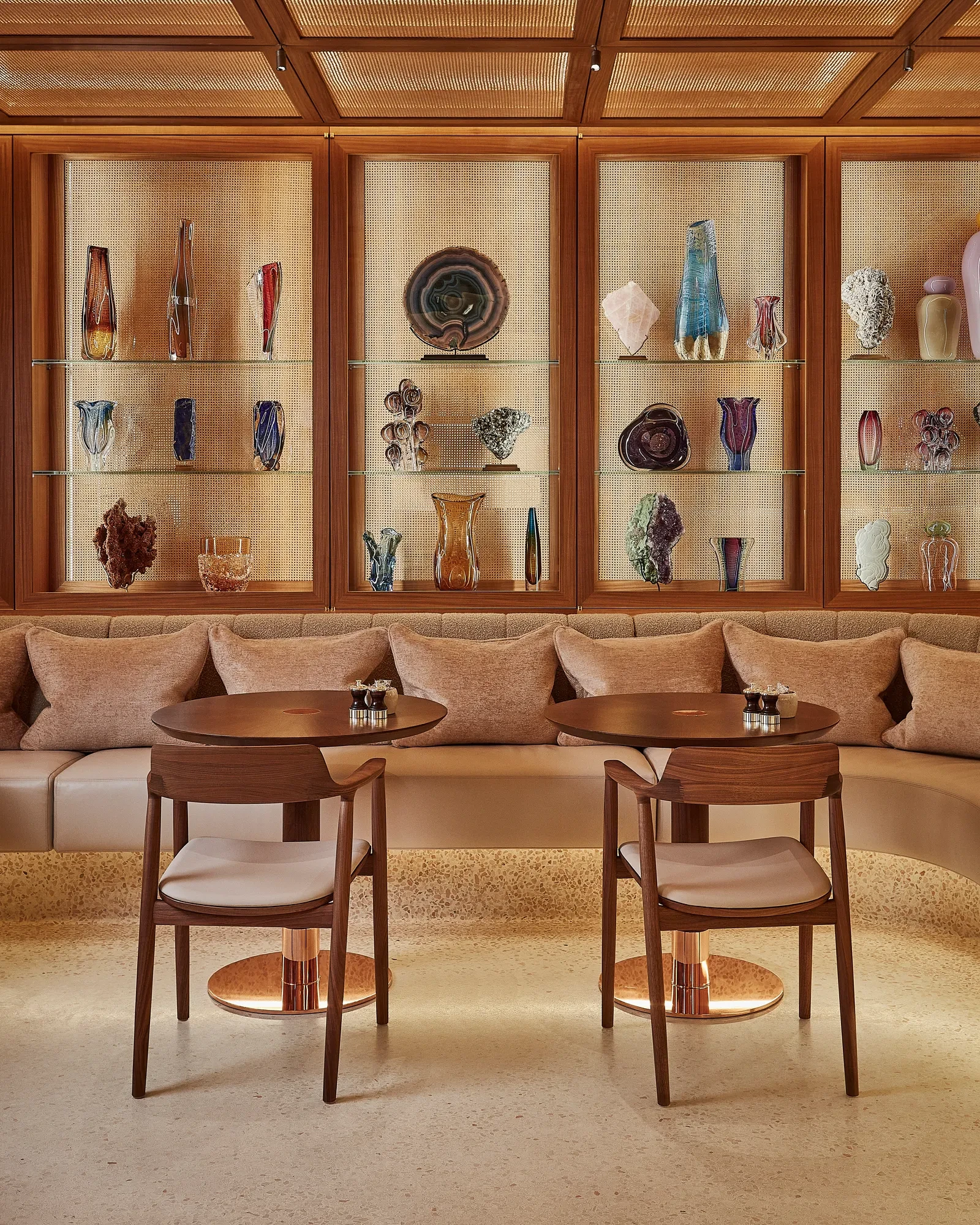 Elegant lounge with glass display cabinets showcasing sculptural vases, paired with wooden tables and upholstered seating.