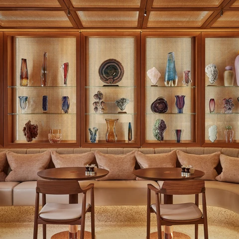 Elegant lounge with glass display cabinets showcasing sculptural vases, paired with wooden tables and upholstered seating.
