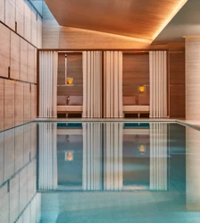 Indoor spa pool with calm water, surrounded by wood-paneled walls and curtained cabanas with soft lighting