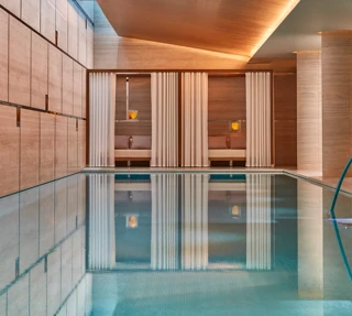 Indoor spa pool with calm water, surrounded by wood-paneled walls and curtained cabanas with soft lighting