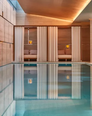 Indoor spa pool with calm water, surrounded by wood-paneled walls and curtained cabanas with soft lighting