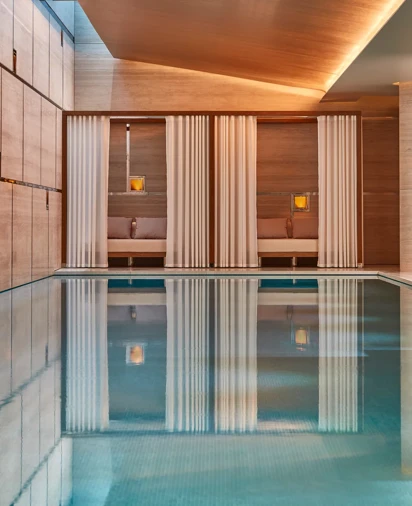 Indoor spa pool with calm water, surrounded by wood-paneled walls and curtained cabanas with soft lighting