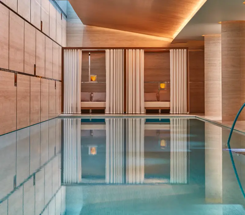 Indoor spa pool with calm water, surrounded by wood-paneled walls and curtained cabanas with soft lighting