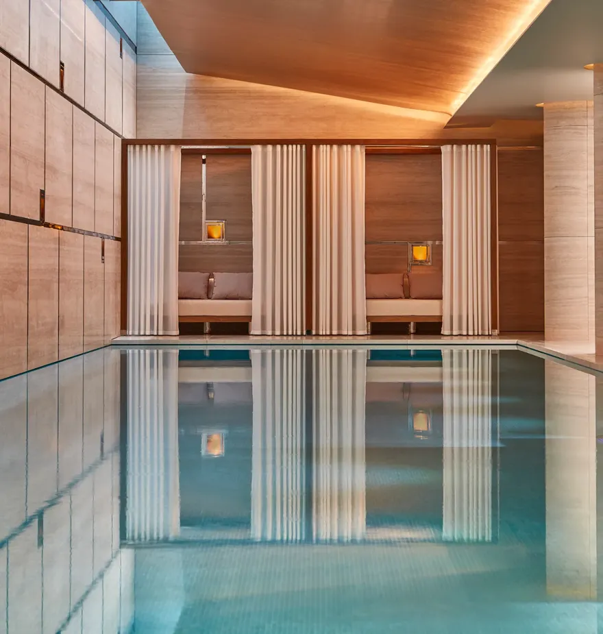 Indoor spa pool with calm water, surrounded by wood-paneled walls and curtained cabanas with soft lighting