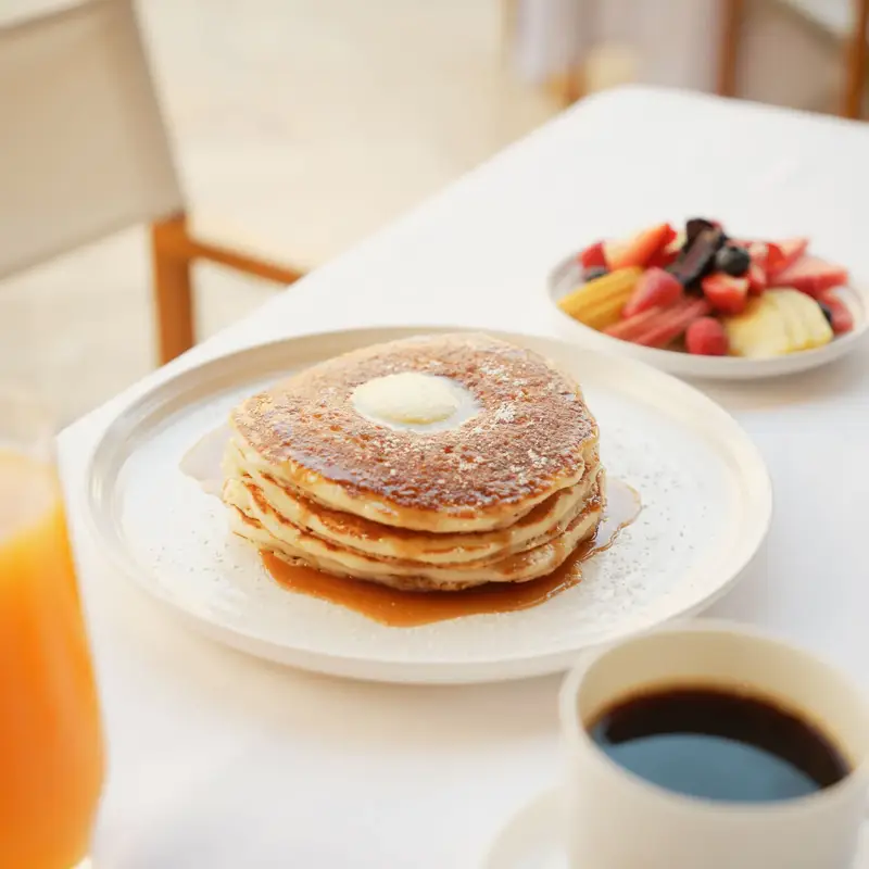 Table with white linen, fresh fruits, coffee, orange juice, and fluffy pancakes.