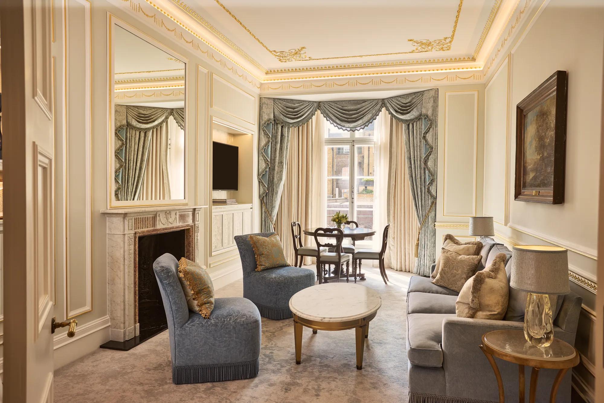 alt text

Living room with blue upholstered seating, marble fireplace and ornate draped windows overlooking the city, with a dining table set by the window.