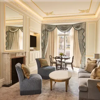 alt text

Living room with blue upholstered seating, marble fireplace and ornate draped windows overlooking the city, with a dining table set by the window.