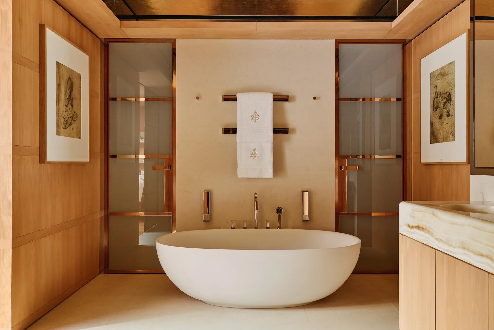 Elegant bathroom at Claridge’s with a freestanding oval bathtub, warm wood panelling, and soft lighting.