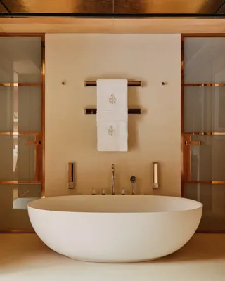 Elegant bathroom at Claridge’s with a freestanding oval bathtub, warm wood panelling, and soft lighting.