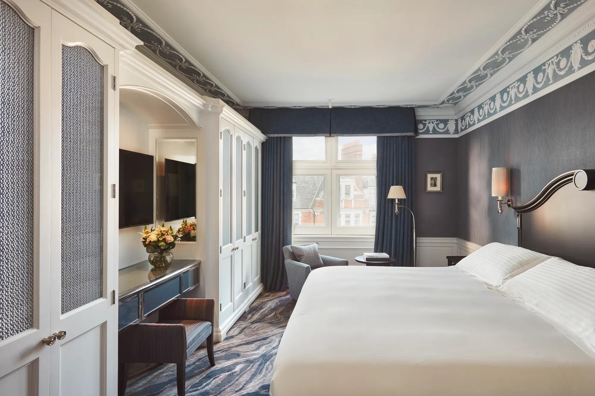 Bedroom with large bed, blue walls and drapes, white wardrobe cabinets, and a seating area by the window.