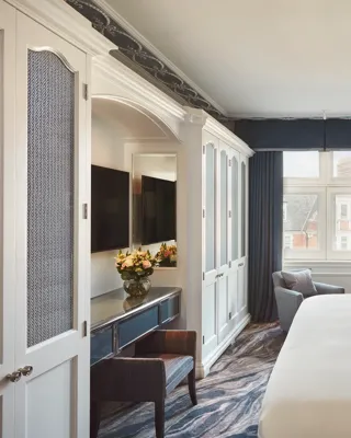 Bedroom with large bed, blue walls and drapes, white wardrobe cabinets, and a seating area by the window.