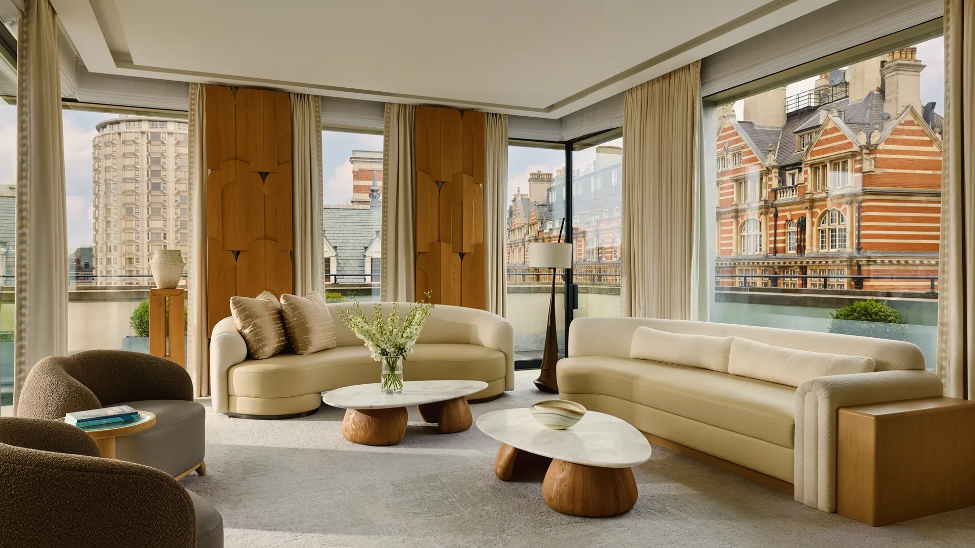Bright penthouse living room with curved sofas, marble tables, and city views through floor-to-ceiling windows