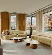 Bright penthouse living room with curved sofas, marble tables, and city views through floor-to-ceiling windows