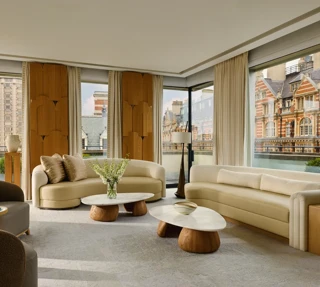 Bright penthouse living room with curved sofas, marble tables, and city views through floor-to-ceiling windows