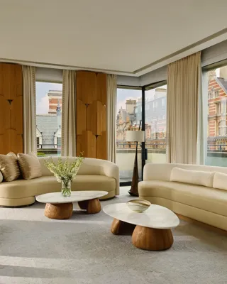 Bright penthouse living room with curved sofas, marble tables, and city views through floor-to-ceiling windows