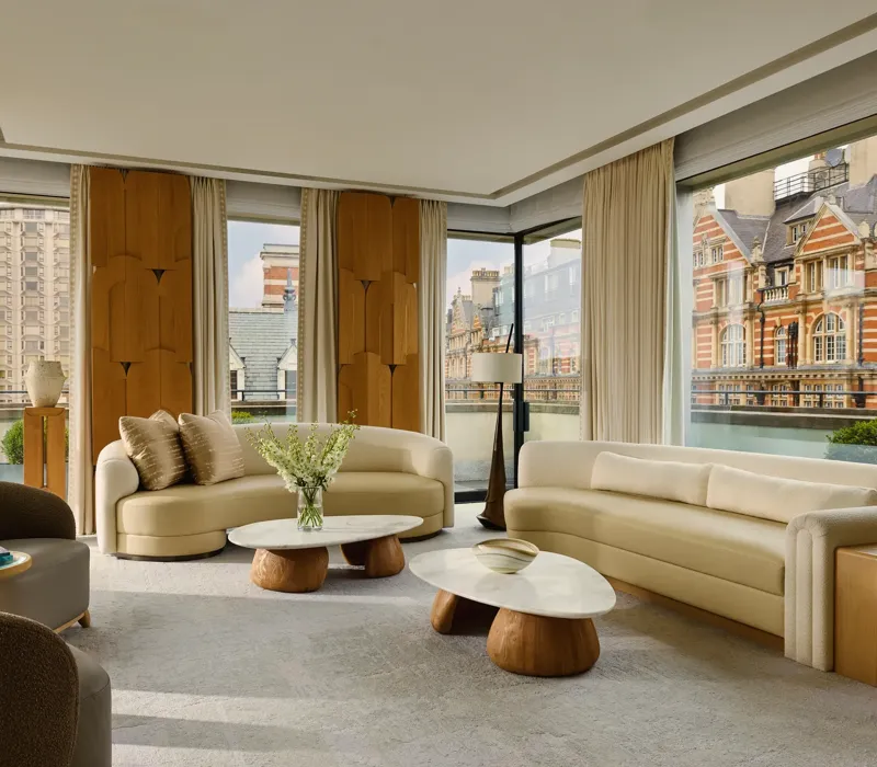 Bright penthouse living room with curved sofas, marble tables, and city views through floor-to-ceiling windows