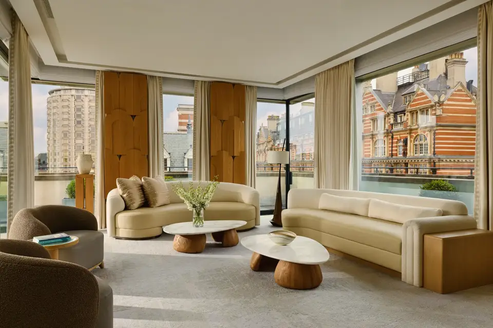 Bright penthouse living room with curved sofas, marble tables, and city views through floor-to-ceiling windows