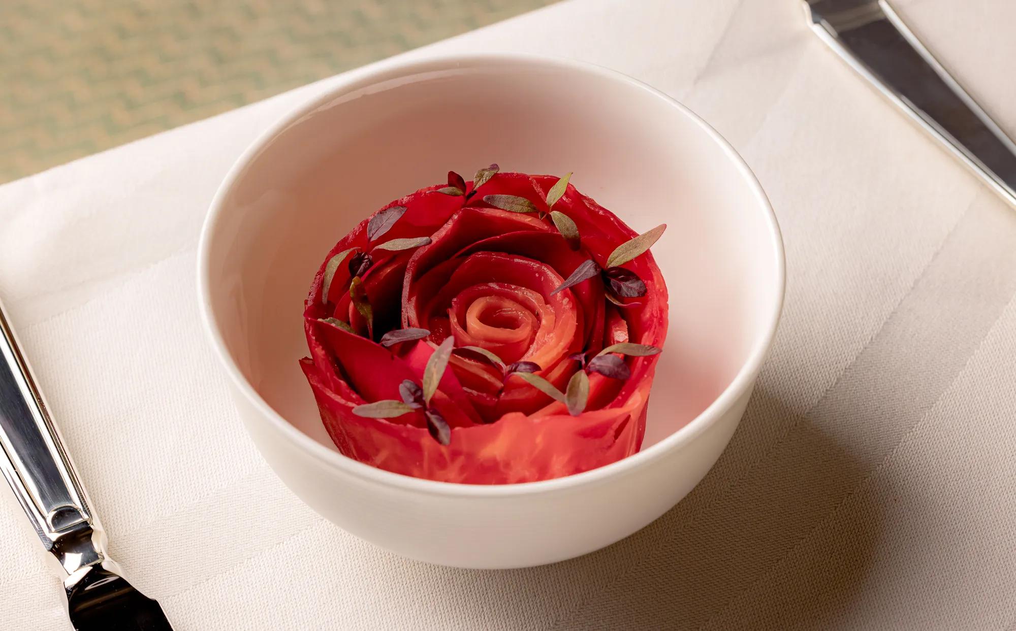 Rose-shaped beetroot dish garnished with micro herbs, presented in a white bowl on a linen tablecloth.