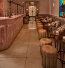 Art Deco bar interior with marble counter, upholstered stools and small tables, featuring stained glass window, decorative lighting and soft ambient glow.
