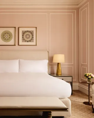 Elegant bedroom with blush-pink panelled walls, a king-size bed with crisp white linens, two golden lamps on bedside tables, and framed artwork above the headboard.