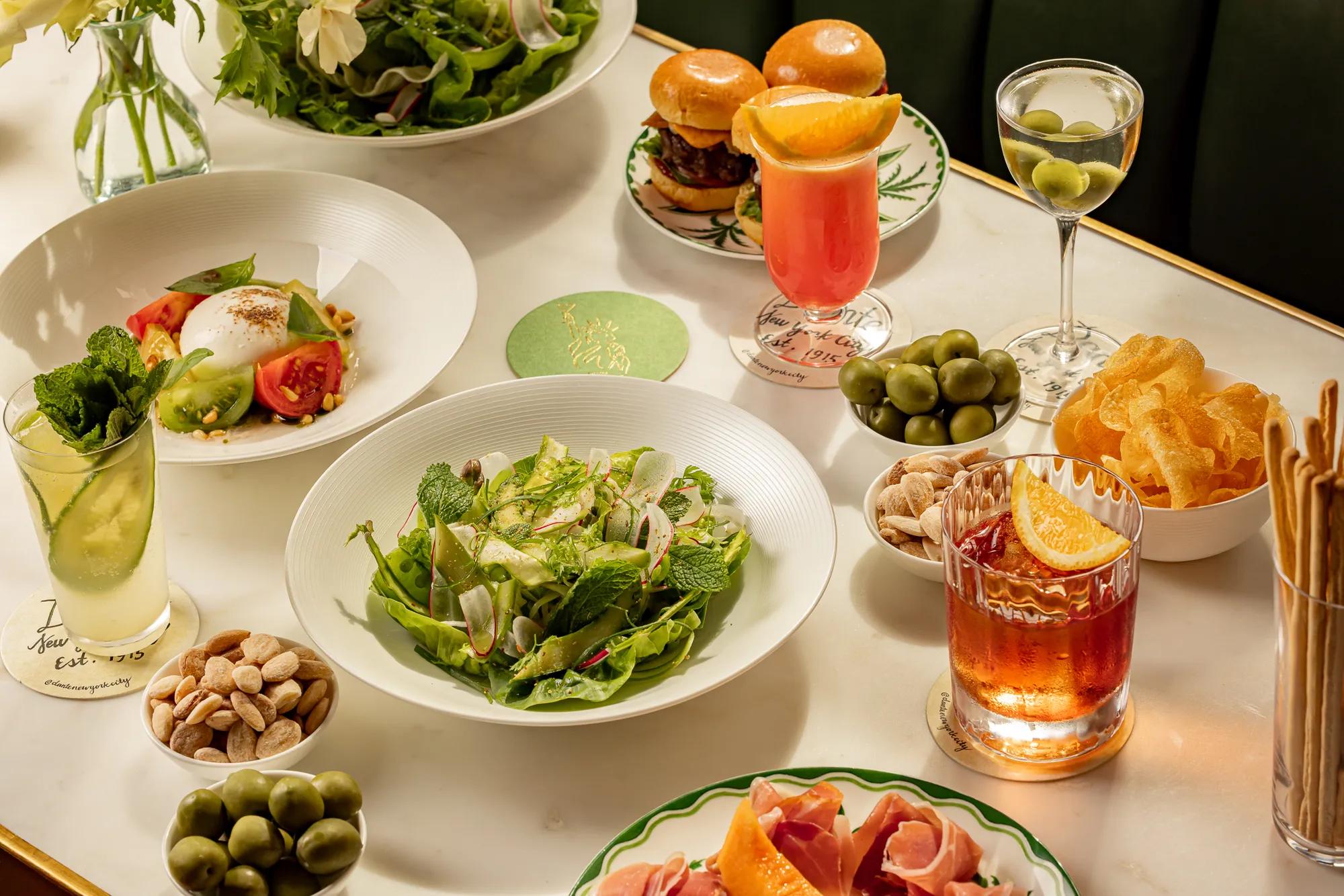 Salads, sliders, cocktails, and bar snacks arranged on an elegant marble restaurant table.