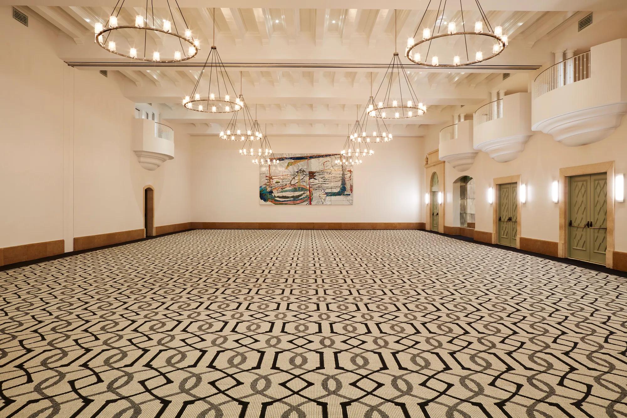 Grand ballroom in Beverly Hills with geometric carpet, multiple ring chandeliers, juliet balconies, and double doors along the side walls.