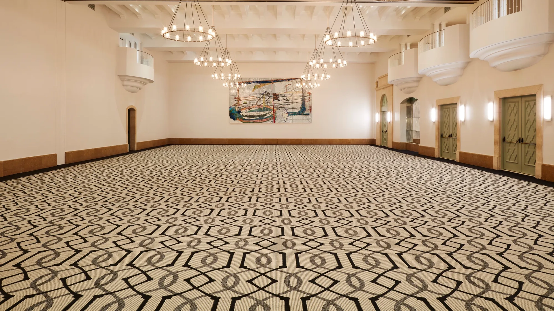 Grand ballroom in Beverly Hills with geometric carpet, multiple ring chandeliers, juliet balconies, and double doors along the side walls.
