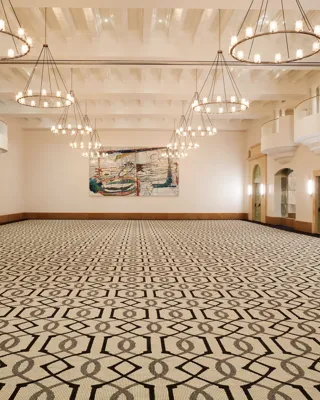 Grand ballroom in Beverly Hills with geometric carpet, multiple ring chandeliers, juliet balconies, and double doors along the side walls.