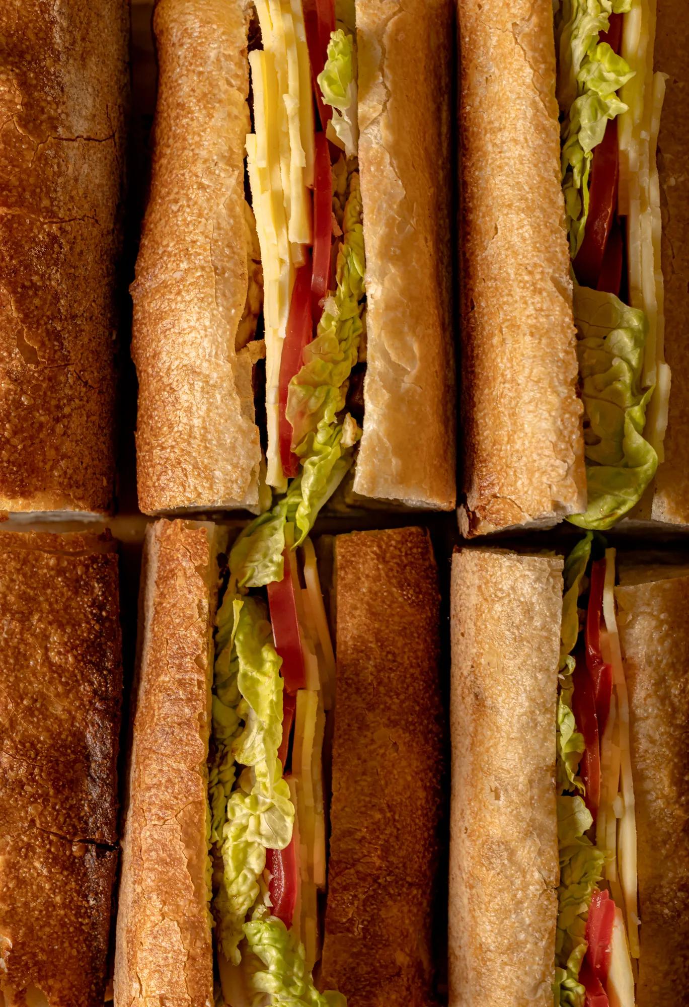 Close-up of stacked toasted sandwiches filled with lettuce, tomato and sliced cheese.
