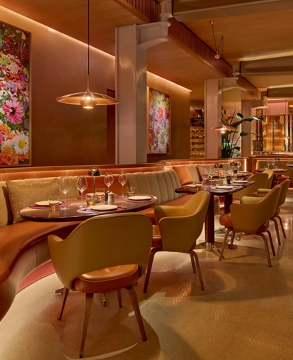 Elegant restaurant interior with upholstered banquettes, set tables, floral artwork, and warm pendant lighting in a refined dining space.