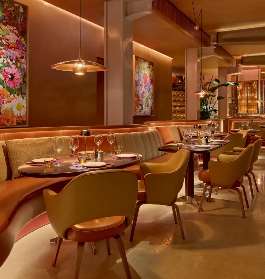 Elegant restaurant interior with upholstered banquettes, set tables, floral artwork, and warm pendant lighting in a refined dining space.