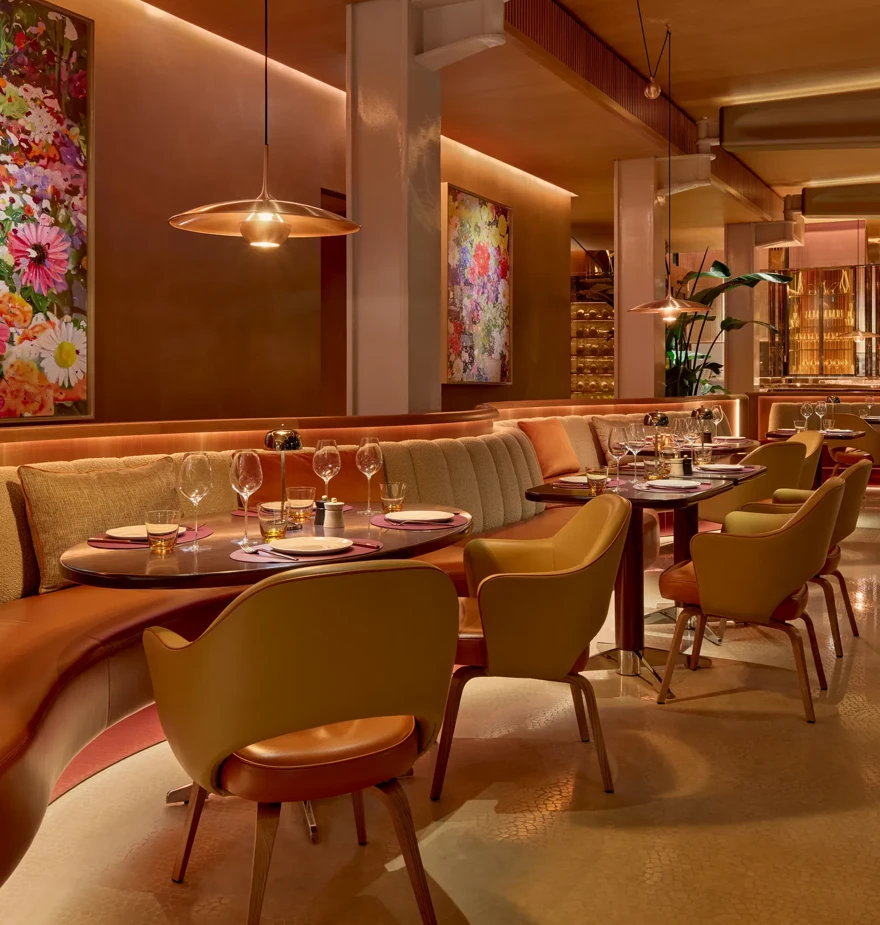 Elegant restaurant interior with upholstered banquettes, set tables, floral artwork, and warm pendant lighting in a refined dining space.