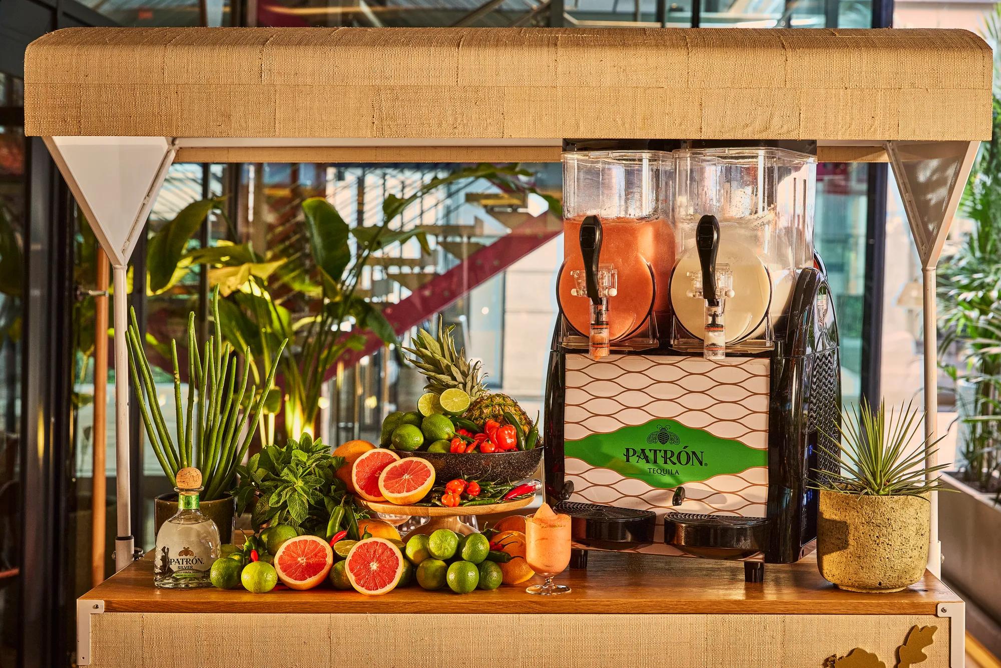 Patrón tequila drinks station with fresh citrus, herbs and tropical garnishes beside frozen cocktails.