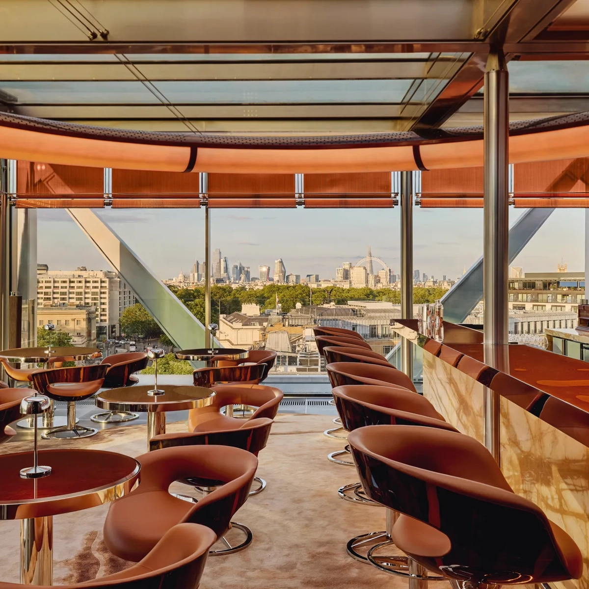 Stylish rooftop bar with caramel leather chairs, marble counter, and panoramic views of London through floor-to-ceiling windows.