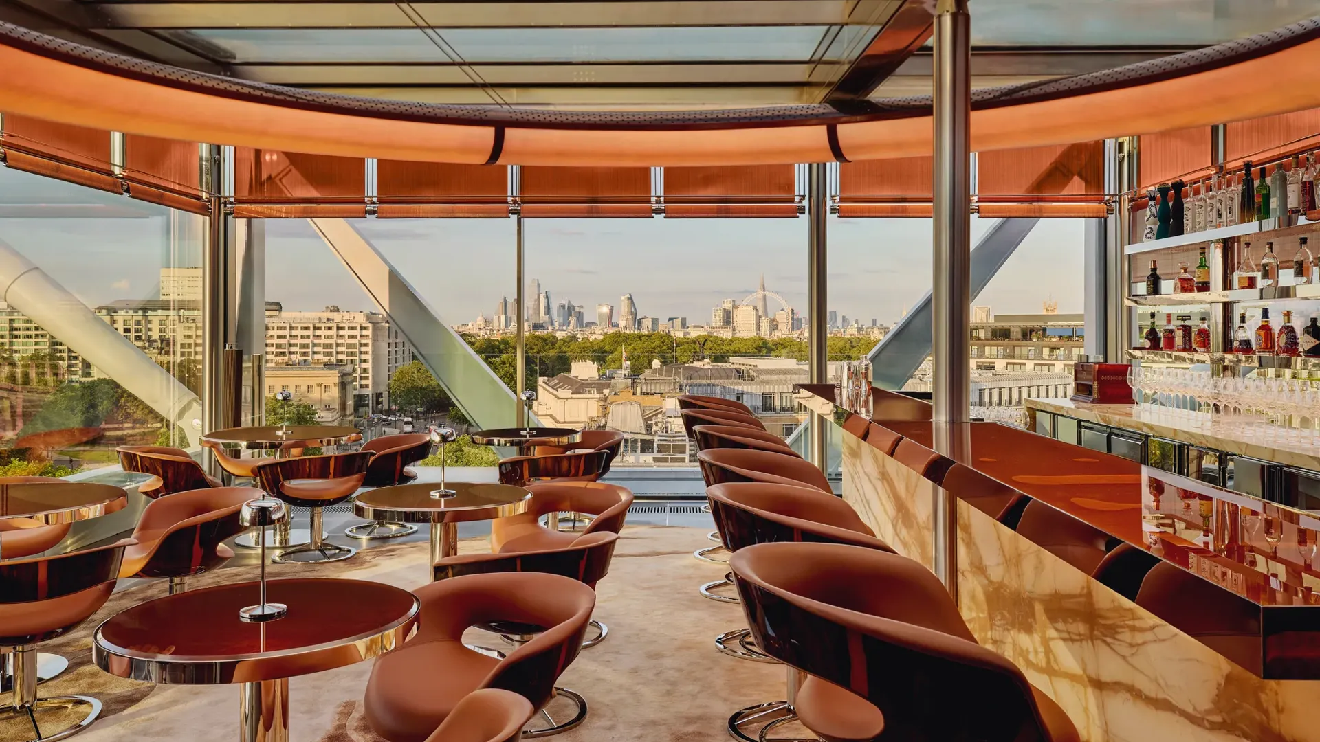 Stylish rooftop bar with caramel leather chairs, marble counter, and panoramic views of London through floor-to-ceiling windows.