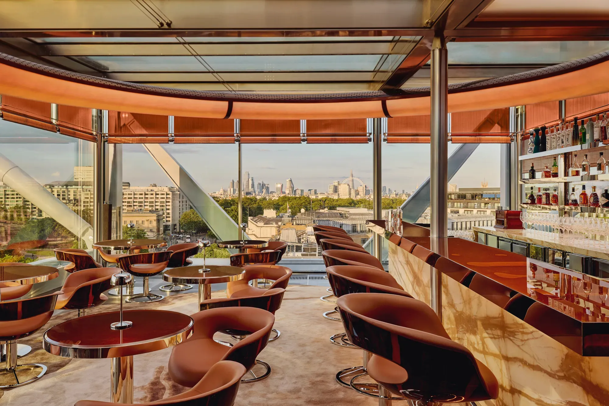 Stylish rooftop bar with caramel leather chairs, marble counter, and panoramic views of London through floor-to-ceiling windows.