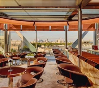 Stylish rooftop bar with caramel leather chairs, marble counter, and panoramic views of London through floor-to-ceiling windows.