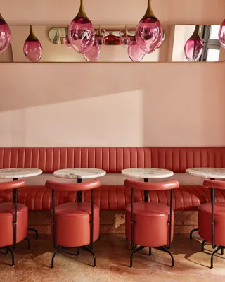 Plush pink banquette seating with round marble tables and pink glass pendant lights in a softly lit café.