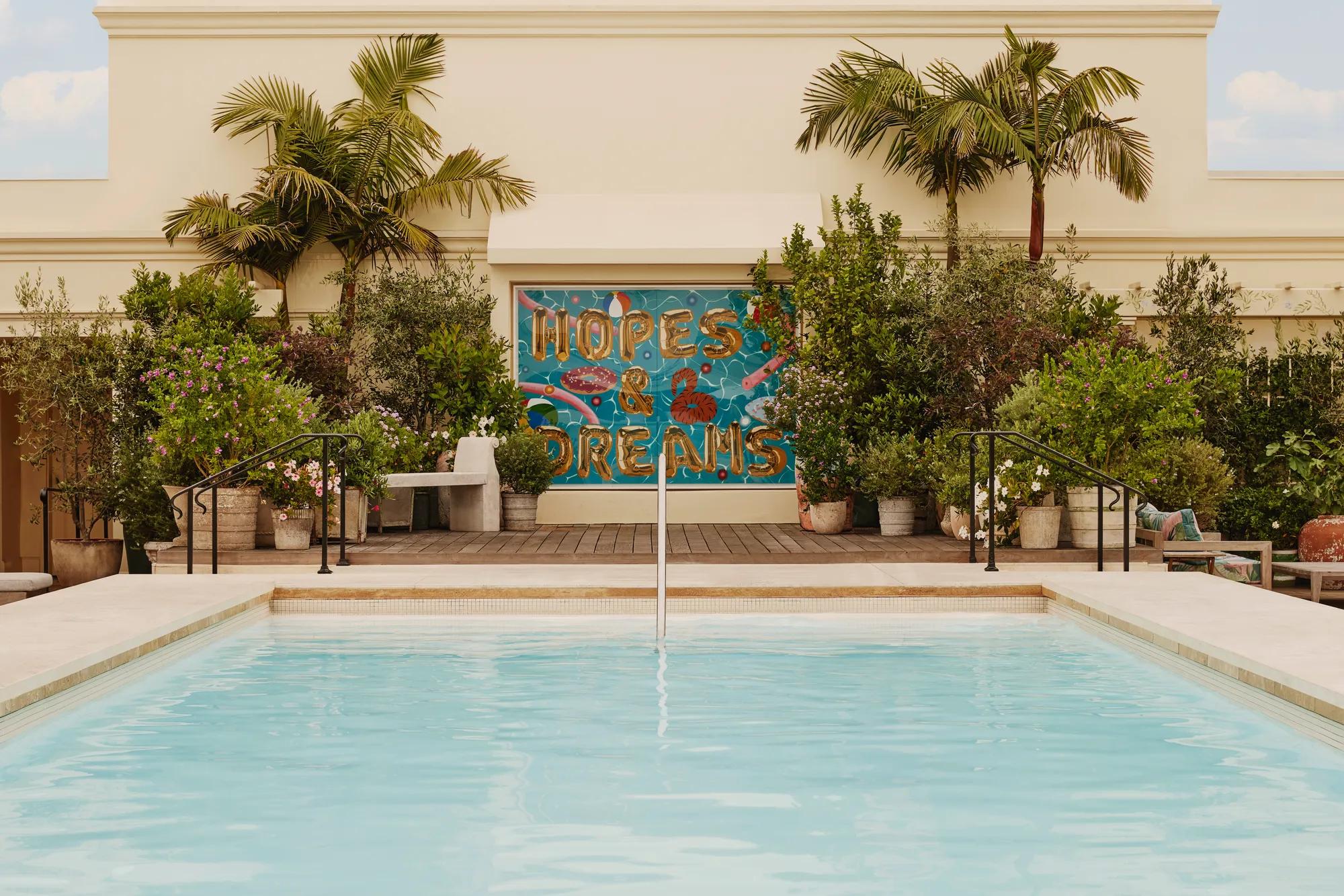 Guest steping from The Maybourne Beverly Hills rooftop pool toward the “Hopes & Dreams” mural, palms and planters behind.