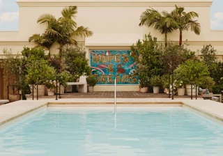 Guest steping from The Maybourne Beverly Hills rooftop pool toward the “Hopes & Dreams” mural, palms and planters behind.
